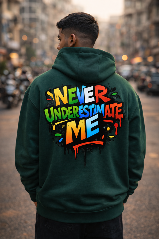 Person wearing a green hoodie with 'Never Underestimate Me' text on the back, standing in an urban setting.