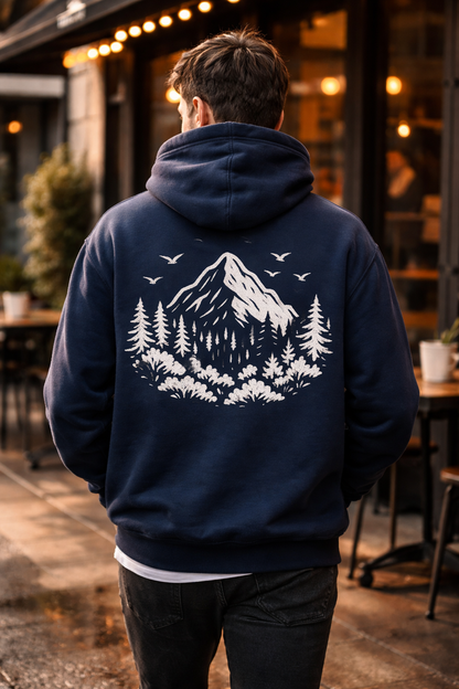 Person wearing a navy hoodie with a mountain and tree design on the back, standing outdoors.